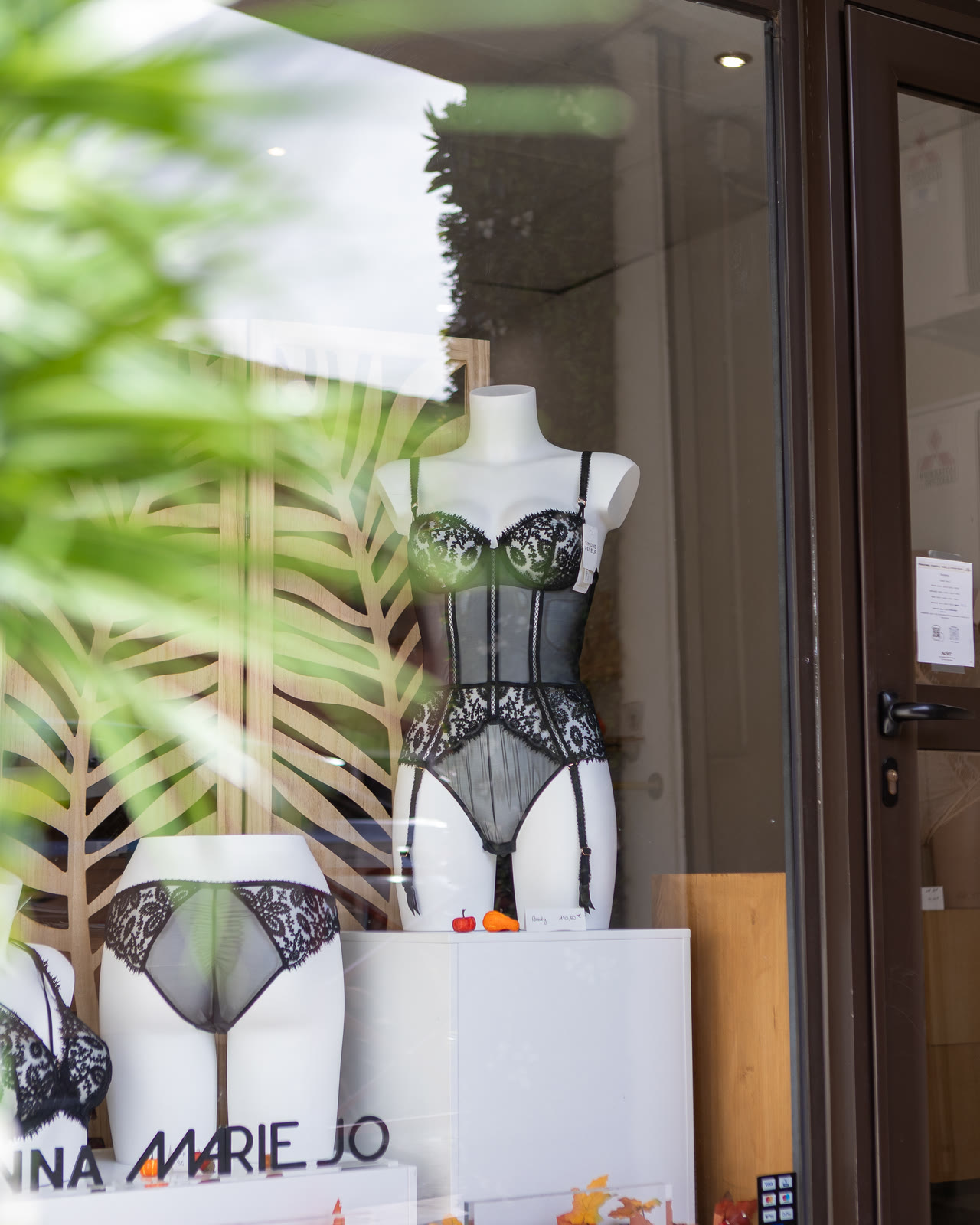 La vitrine de la boutique, aperçue à travers les murs végétaux — un body en dentelle Marie Jo